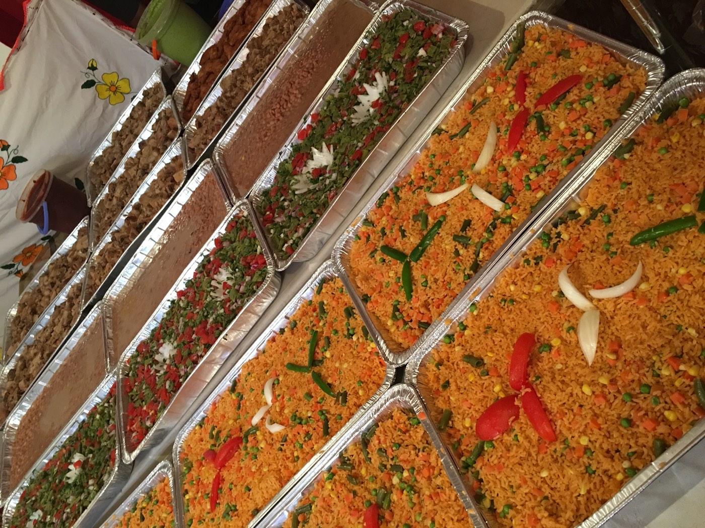 Mesa de catering con charolas de arroz, frijoles y guarniciones